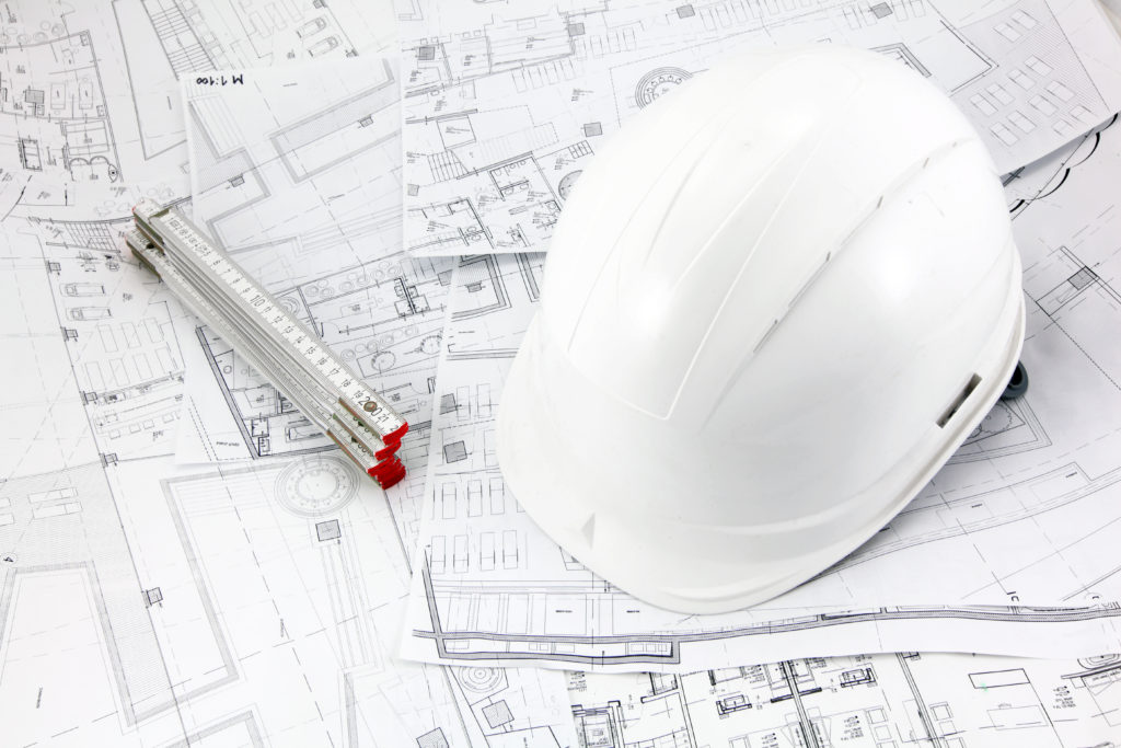 Blueprints helmet and meter at the construction site Pre-construction services on a project featuring commercial construction blueprints and a hard hat.