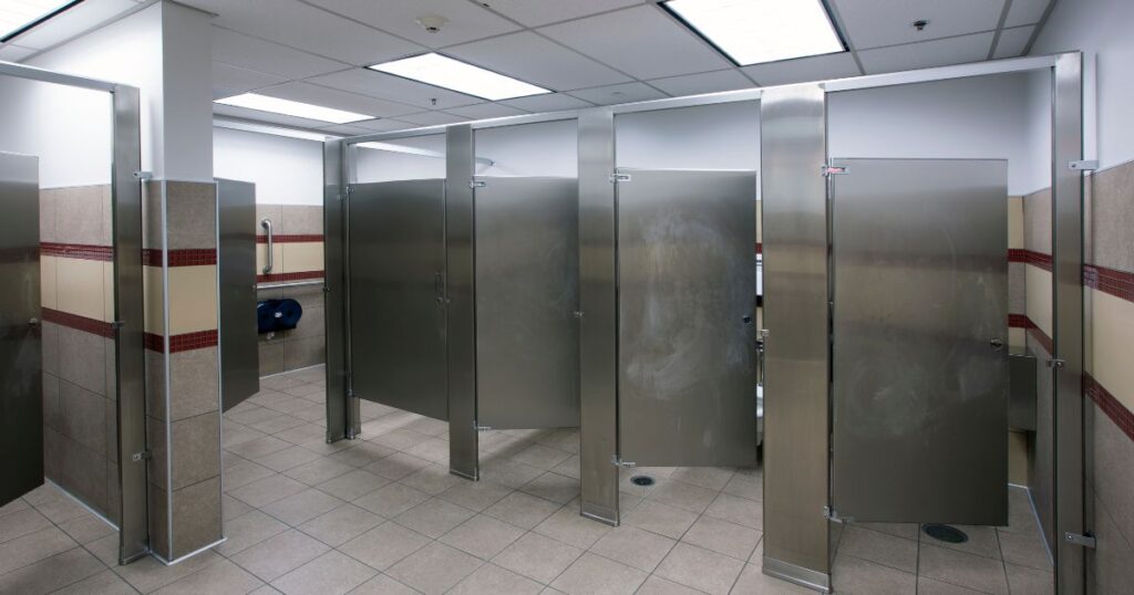 The UFC gym was built by Hilbers with low-flow toilets for water conservation, an important sustainable practice in construction. The ground is brown, the walls have a red and tan stripe, and the stalls are grey. 