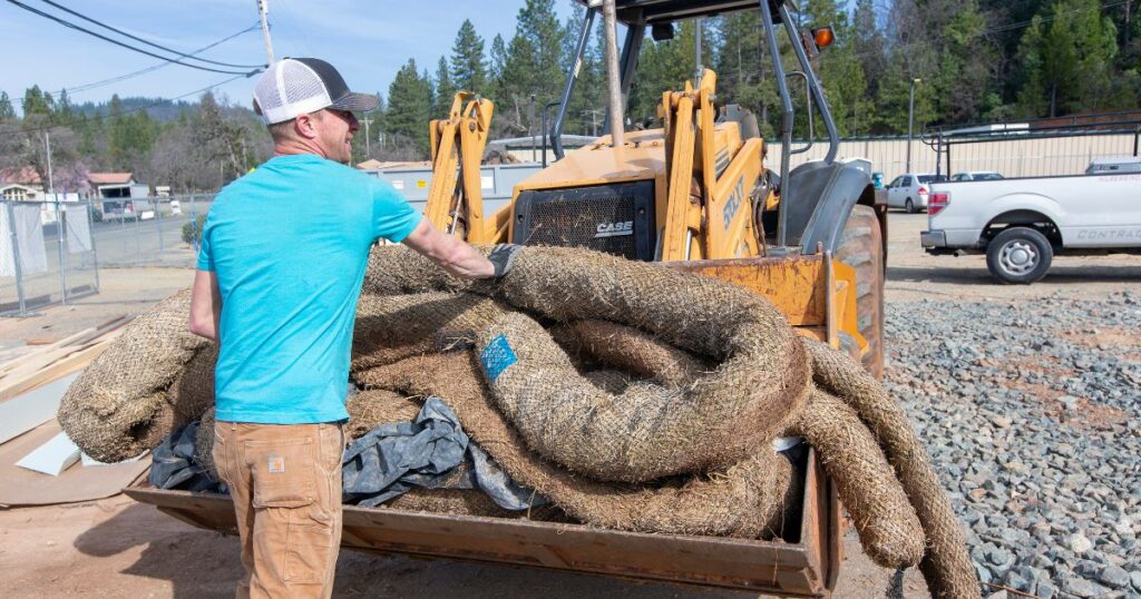 A Hilber's team member in blue shirt puts straw wattles in a tractor to recycle while on a green construction site. 