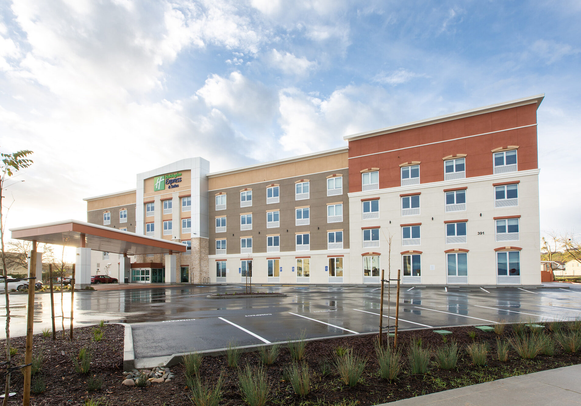 Exterior of a Holiday Inn Express under a cloudy blue sky. The parking lot in front is wet.