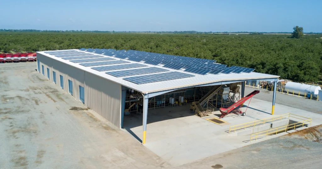 A steel building built by Hilbers Construction with Solar panels on top to meet Green building standards. A field of trees is in the background with a blue sky.