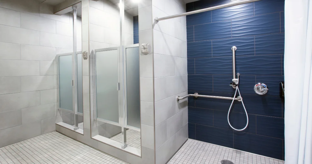 Gym showers, two normal stalls that are white, 1 handicap stall with a navy wall, the floor and other walls are white. These showers meet Green Building Standards.