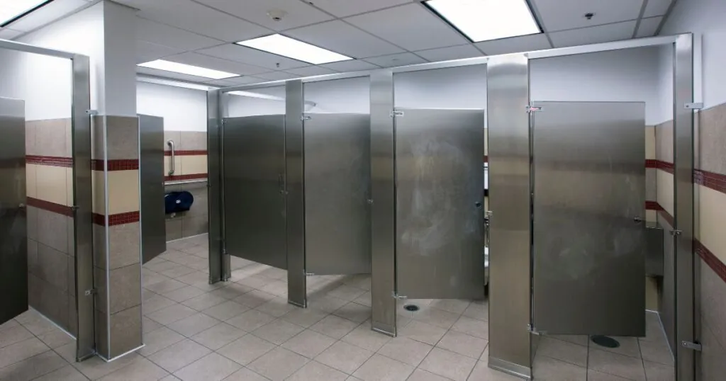 The UFC gym was built by Hilbers with low-flow toilets for water conservation, an important sustainable practice in construction. The ground is brown, the walls have a red and tan stripe, and the stalls are grey.