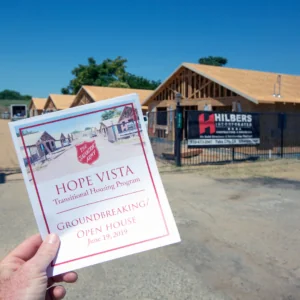 Hand holding a flyer reading Hope Vista in front of an under-construction building.