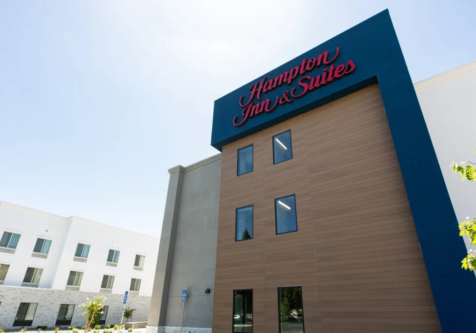 A low angle view of a building with the Hampton Inn & Suites logo on the top. The sky is clear and blue.