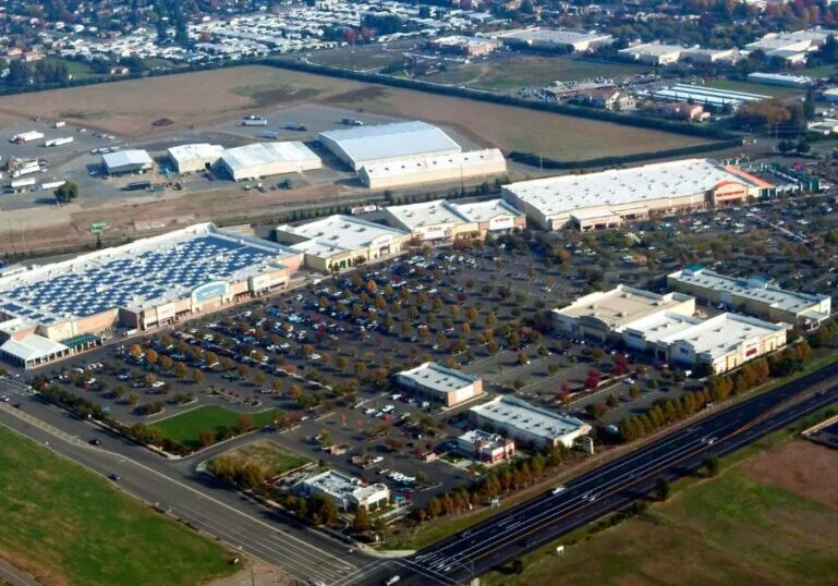 A shopping center built by Hilbers. It is an aerial view with a parking lot closest and a group of light-colored buildings with solar panels farther back.