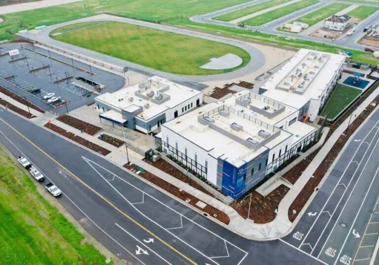 Aerial view of a school on the corner of two roads. Behind the school is a track and green fields.